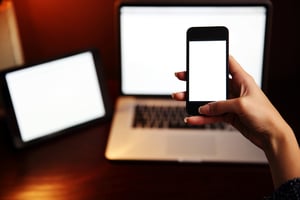 Closeup image of a female hand holding smartphone with tablet computer and laptop background-1