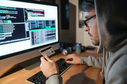 Concentrated young hacker in glasses stealing money from different credit cards sitting in dark room-1